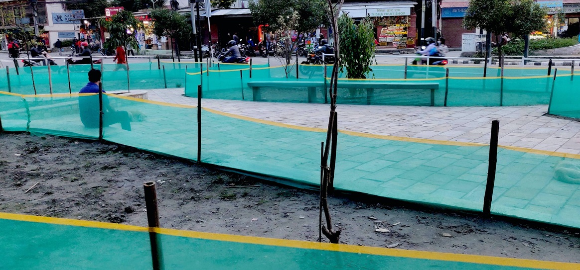 a man sitting in the middle lane by a street side and the area is surrounded by plastic green barriers